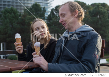 Happy father and daughter eating ice cream sitting in city street cafe outdoors. Happy family Happy father and daughter eating ice cream sitting in city street cafe outdoors. Happy family 129017688