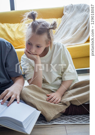 Clever little girl sitting on sofa reading book at home. Childhood and people concept 129018087