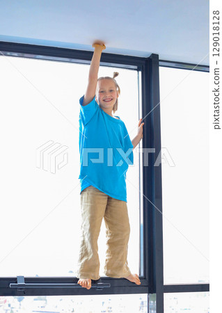 Joyful little girl having fun on window indoor. Kid 6 years old portrait 129018128