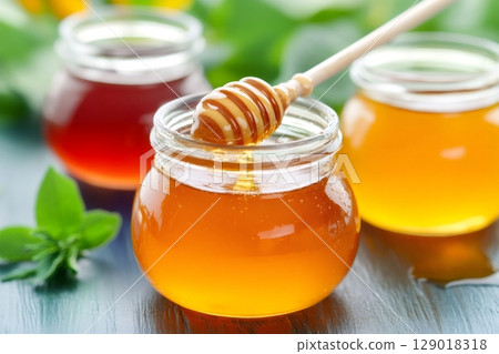 Honey dripping from wooden dipper into glass jar on table with mint leaves 129018318