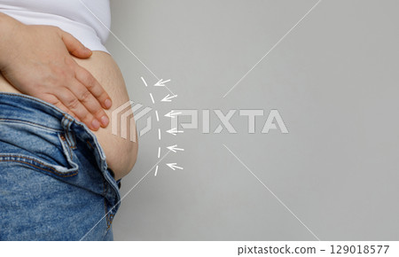 Female hand and belly close up on gray background. Weight loss and aesthetic surgery concept. 129018577