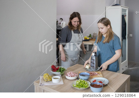 Little daughter and her mother cooking in domestic kitchen together, family lifestyle portrait 129018864