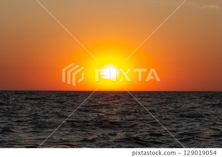 A vibrant sunset over the sea with warm colors reflecting on the gentle waves A vibrant sunset over the sea with warm colors reflecting on the gentle waves 129019054