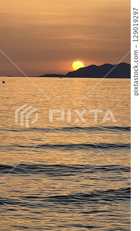 Serene Sunset Over Calm Ocean With Distant Mountains 129019297