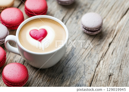 Delicious creamy beige latte with heart design accompanied by colorful macarons on rustic wooden table Delicious creamy beige latte with heart design accompanied by colorful macarons on rustic wooden table 129019945