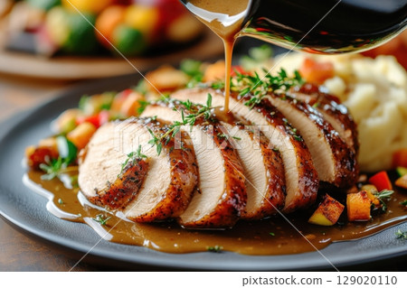 Rich golden-brown gravy poured over tender slices of roast turkey with festive sides in a cozy Thanksgiving setting 129020110