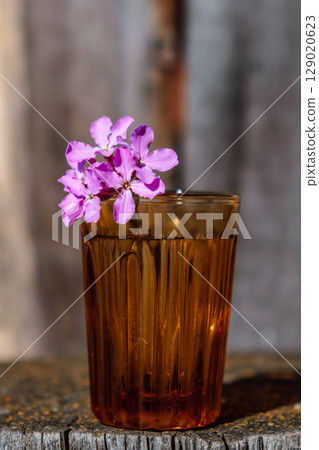 bright purple flower in an amber glass on rustic wooden surface. vertical. closeup. 129020623