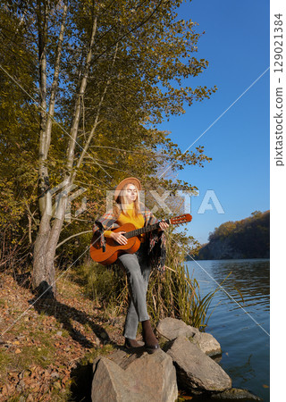 Portrait of smiling caucasian artist plays wooden acoustic guitar in autumnal park. Young songwriter plays string musical instrument hobby outside in nature fall time. Audio music healing 129021384