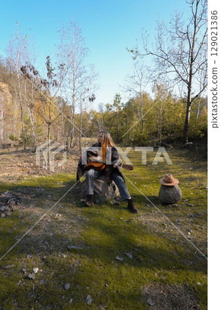 Portrait of smiling caucasian artist plays wooden acoustic guitar in autumnal park. Young songwriter plays string musical instrument hobby outside in nature fall time. Audio music healing Portrait of smiling caucasian artist plays wooden acoustic guitar in autumnal park. Young songwriter plays string musical instrument hobby outside in nature fall time. Audio music healing 129021386