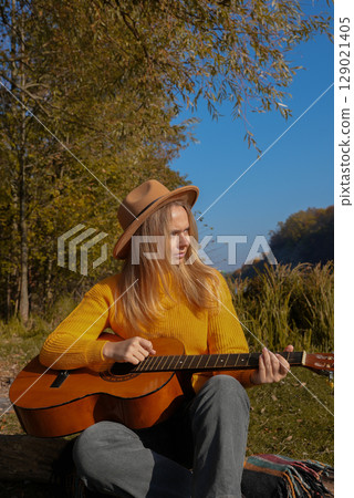 Portrait of smiling caucasian artist plays wooden acoustic guitar in autumnal park. Young songwriter plays string musical instrument hobby outside in nature fall time. Audio music healing 129021405