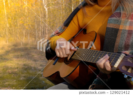 Close up of hands playing string guitar outdoors in autumn forest. Concept of sound therapy, mental health and wellness rituals. Calmness tranquility audio-sensory practices. Aura farming energy 129021412