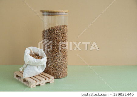 Refillable glass jar with raw buckwheat porridge and cotton bag. Copy space Refill product format eco-friendly living. Filling reusable container Whole spelt grain species. High protein fiber-rich Refillable glass jar with raw buckwheat porridge and cotton bag. Copy space Refill product format eco-friendly living. Filling reusable container Whole spelt grain species. High protein fiber-rich 129021440