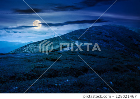 wonderful mountain landscape with rolling hills at night. summer outdoor adventure with path to the top in full moon light. dark blue sky with clouds. alpine scenery at midnight. astrology background 129021467