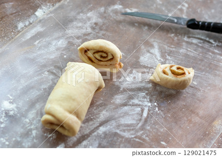 Dough, rolled into roll, is cut into slices for baking cinnamon buns Dough, rolled into roll, is cut into slices for baking cinnamon buns 129021475
