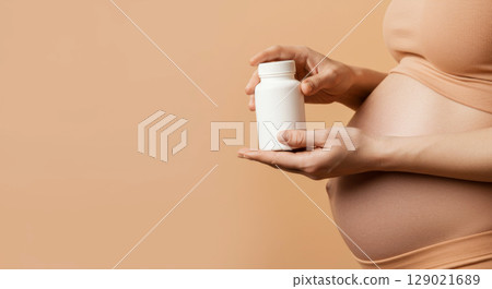 Pregnant woman holding a white medicine bottle. Prenatal care, pregnancy vitamins, and maternal health. 129021689