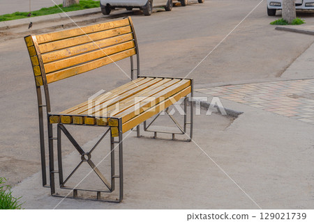 Free empty wooden bench with a metal frame installed on the walking place of the street next to the roadway with copy space. Public walking spaces without people 129021739