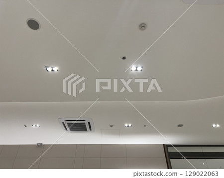 Functional and modern white ceiling with recessed lighting, air conditioner, security camera, smoke detector, and speaker creating secure and comfortable atmosphere 129022063