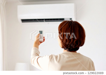 A woman adjusting the temperature with an air conditioner remote control 129022089
