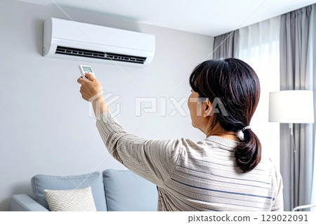 A woman adjusting the temperature with an air conditioner remote control 129022091