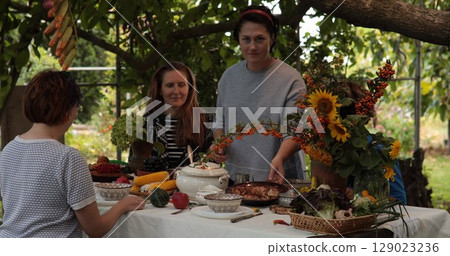 Group of friends celebrate Thanksgiving in a beautiful garden filled with autumn colors and freshly prepared dishes. Decorated table showcases seasonal produce and floral arrangements. Group of friends celebrate Thanksgiving in a beautiful garden filled with autumn colors and freshly prepared dishes. Decorated table showcases seasonal produce and floral arrangements. 129023236