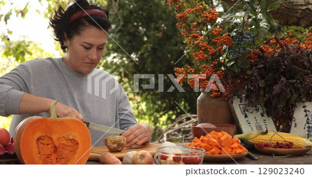 Woman is focused on preparing Thanksgiving meal in outdoor kitchen, chopping fresh vegetables and fruits. Surroundings include autumn foliage and harvest decorations, enhancing festive mood. Woman is focused on preparing Thanksgiving meal in outdoor kitchen, chopping fresh vegetables and fruits. Surroundings include autumn foliage and harvest decorations, enhancing festive mood. 129023240