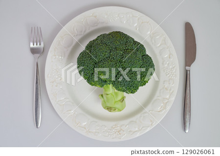 Raw broccoli on white plate with fork and knife Raw broccoli on white plate with fork and knife 129026061