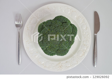 Raw broccoli on white plate with fork and knife 129026092