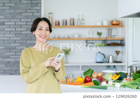 Middle-aged woman using a smartphone in the kitchen 129026260