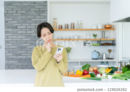 Middle-aged woman using a smartphone in the kitchen Middle-aged woman using a smartphone in the kitchen 129026262