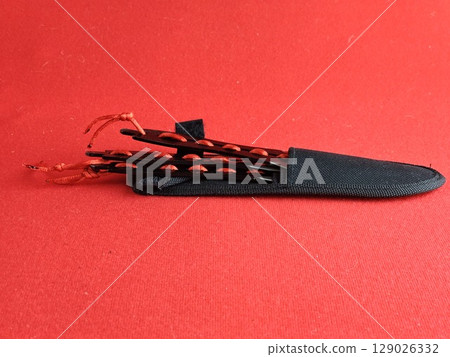 A set of several throwing knives in a case for combat training and sport throwing on a red background. A set of several throwing knives in a case for combat training and sport throwing on a red background. 129026332