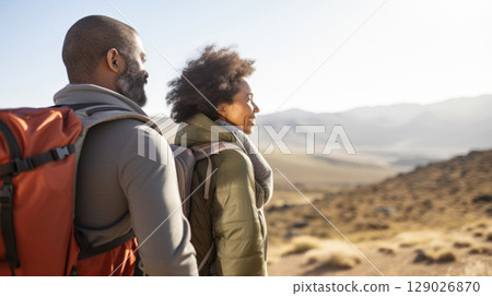 Mixed race couple hiking in desert landscape, wearing winter gear, smiling 129026870