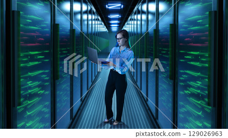 Woman with laptop standing in glowing 3D server corridor 129026963