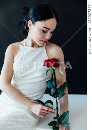 woman in a white dress holding a red rose in her hand 129027263