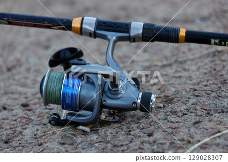 A Close-Up Look at a Fishing Reel and Rod Set Against a Rocky Surface, Perfect for Angling Enthusiasts and Outdoor Activity Lovers Alike, Showcasing Fishing Gear in Detail 129028307