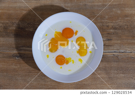 A Delicious Display of Fresh Egg Yolks and Cream Blended Together in a White Bowl Arranged on a Rustic Wooden Table for a Culinary Presentation, Perfect for Breakfast or Baking. 129028534