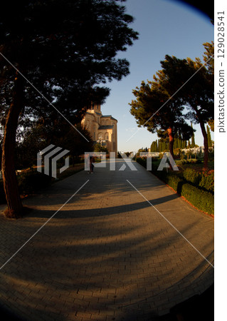 A Tranquil Pathway Leading Towards a Historic Building Surrounded by Lush Greenery Under a Clear Blue Sky at Sunset, Exuding Serenity and Natural Beauty 129028541