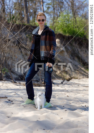 A Young Woman Enjoys a Beautiful Day Outdoors with Her Playful White Cat on a Sandy Beach Surrounded by Lush Greenery and Tall Trees Under a Clear Blue Sky A Young Woman Enjoys a Beautiful Day Outdoors with Her Playful White Cat on a Sandy Beach Surrounded by Lush Greenery and Tall Trees Under a Clear Blue Sky 129028661