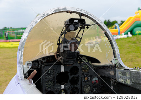 Cockpit of a Vintage Aircraft Showcasing Historical Aviation Instruments and Design, Set Against a Fun Land of Colorful Inflatables and Play Equipment in the Background 129028812