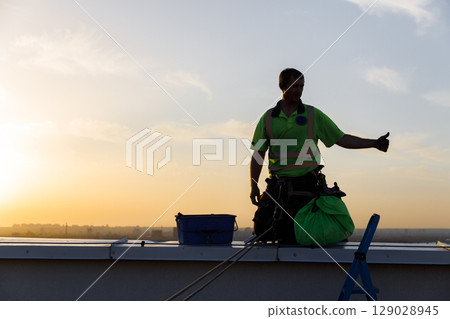 Construction Worker on Rooftop at Sunset: Celebrating Achievement with a Thumbs Up Gesture, Embracing Hard Work and Dedication While Dressed in Safety Gear Construction Worker on Rooftop at Sunset: Celebrating Achievement with a Thumbs Up Gesture, Embracing Hard Work and Dedication While Dressed in Safety Gear 129028945