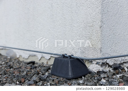 Detailed Close-Up of a Cable Holder Secured to a Wall, Embedded in Gravel Surrounding, Highlighting Practical Elements of Exterior Installation for Electrical Wiring Solutions 129028980