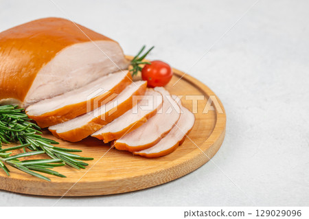 Sliced smoked turkey breast on a wooden board with fresh rosemary and cherry tomato on a light background. top view. copy space. Sliced smoked turkey breast on a wooden board with fresh rosemary and cherry tomato on a light background. top view. copy space. 129029096