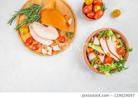 Fresh salad with sliced smoked turkey breast, cherry tomatoes, and olives served alongside a wooden board of turkey and herbs. top view. copy space. Fresh salad with sliced smoked turkey breast, cherry tomatoes, and olives served alongside a wooden board of turkey and herbs. top view. copy space. 129029097