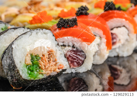 An assorted variety of colorful sushi rolls is displayed on a glossy black surface, showcasing vibrant toppings and fresh ingredients An assorted variety of colorful sushi rolls is displayed on a glossy black surface, showcasing vibrant toppings and fresh ingredients 129029113