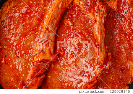 Close-up of raw pork chops coated in a spicy red marinade with visible pepper and oil Close-up of raw pork chops coated in a spicy red marinade with visible pepper and oil 129029146