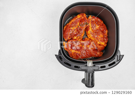 Top view of marinated pork steaks in an air fryer basket on a light surface with copy space Top view of marinated pork steaks in an air fryer basket on a light surface with copy space 129029160