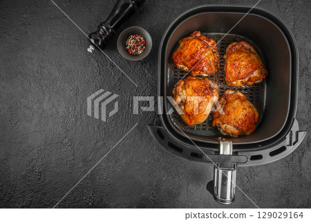 Roasted chicken thighs cooked in an air fryer basket with pepper mix and grinder on a dark textured background. top view. copy space 129029164