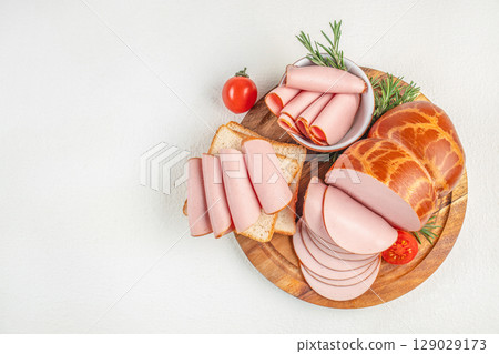 Assorted bologna slices with bread, tomato, and rosemary served on a wooden board. top view. copy space Assorted bologna slices with bread, tomato, and rosemary served on a wooden board. top view. copy space 129029173