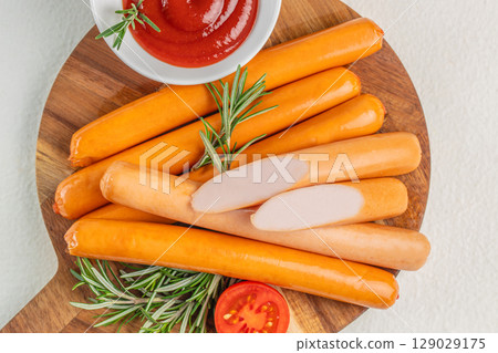 Close-up of uncooked sausages with ketchup, rosemary, and tomato on a wooden cutting board Close-up of uncooked sausages with ketchup, rosemary, and tomato on a wooden cutting board 129029175