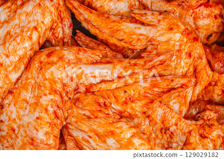 Raw chicken wings coated in bright orange spicy marinade, close-up texture background 129029182