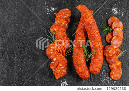 Cured smoked sausages and sliced spicy salami arranged with rosemary sprigs on a dark textured background. Top view Cured smoked sausages and sliced spicy salami arranged with rosemary sprigs on a dark textured background. Top view 129029288